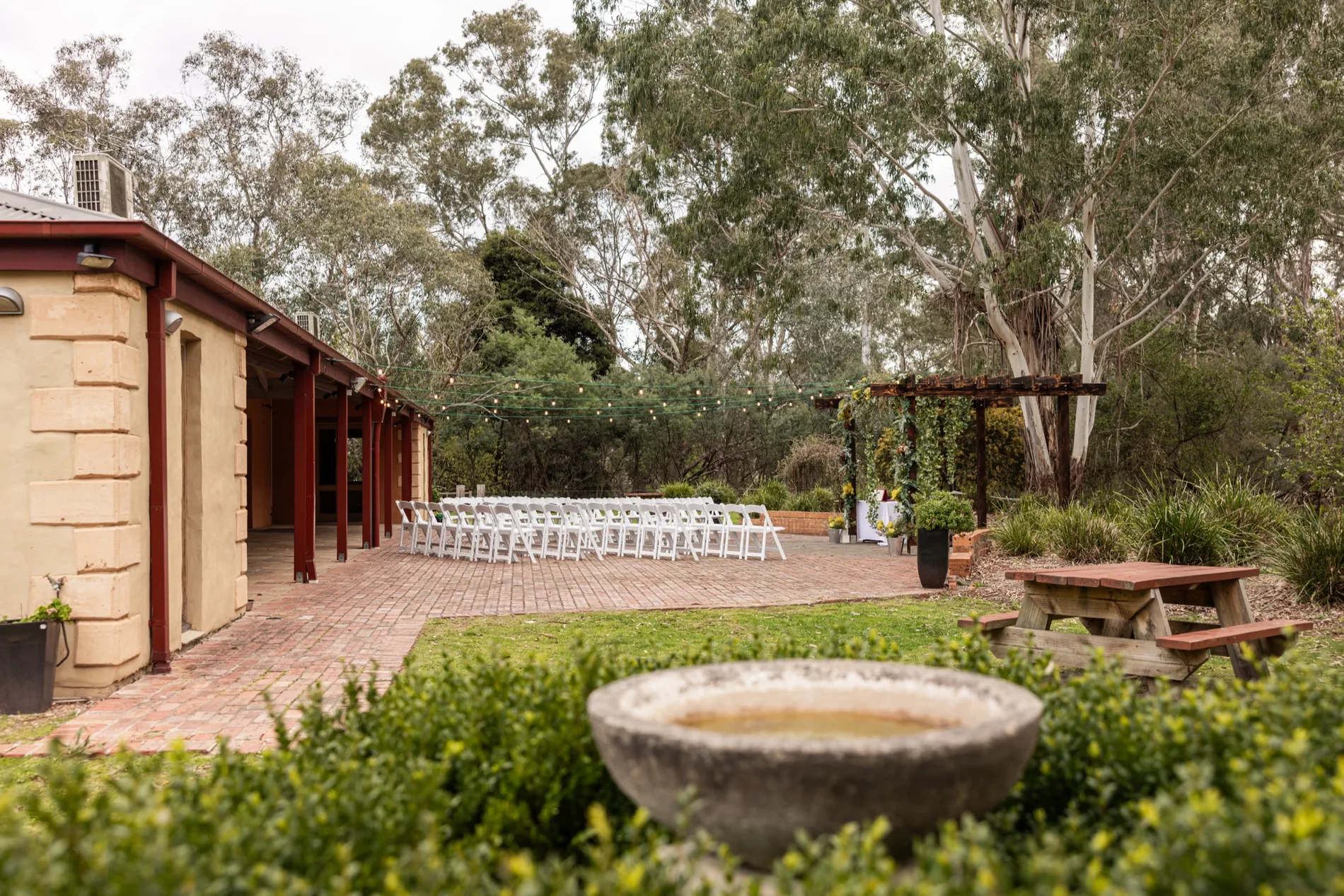 Chairs set out in rows for a ceremony in the courtyard, with the bush behind.