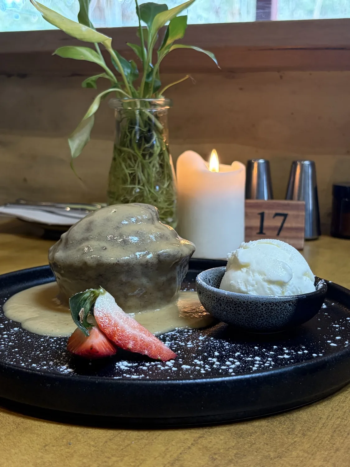 Sticky date pudding under butterscotch sauce with a scoop of ice cream, beside a candle.