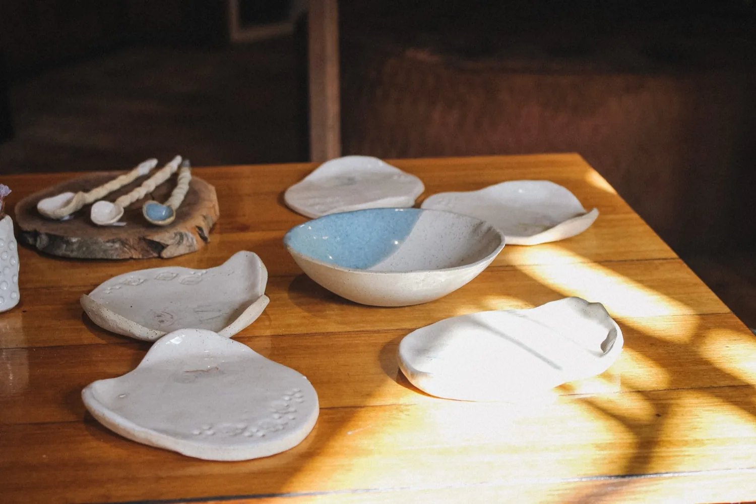 Hand-thrown ceramic dishes on a timber table in window light.